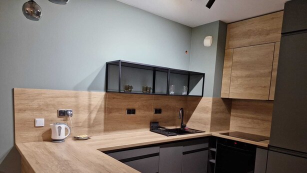 A modern kitchen with a wooden countertop, a built-in sink, and dark cabinetry. - Cozy 1-bedroom apartment in lovely Warszawa with WiFi (Warszawa)