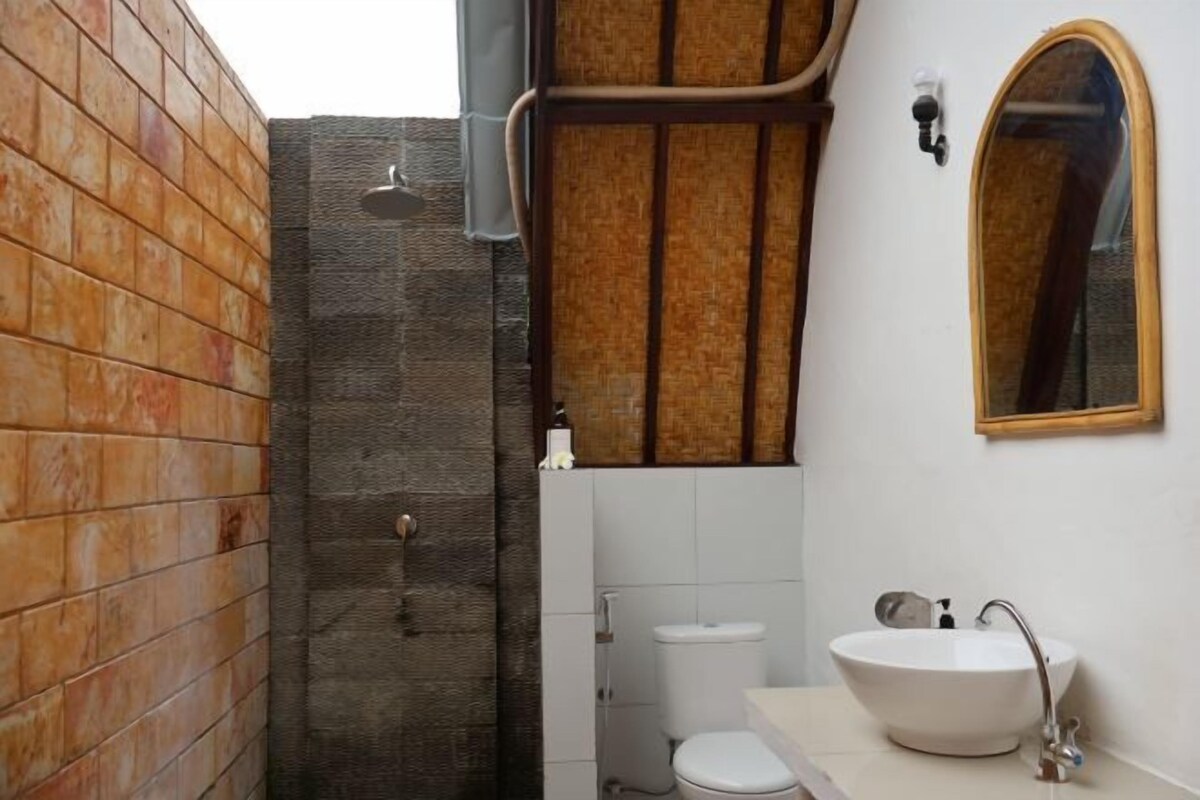 Un baño con lavamanos blanco, espejo y zona de ducha con pared de azulejos.