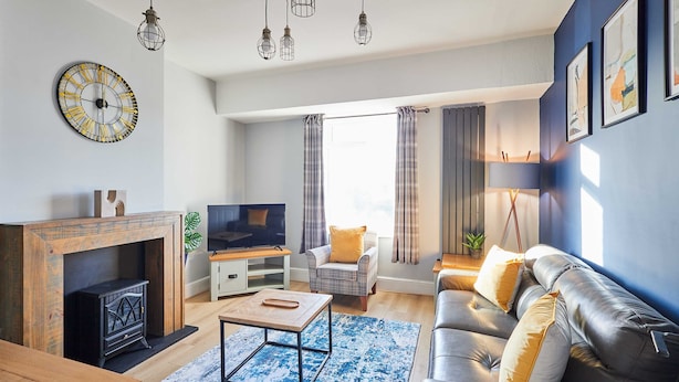 A modern living room with a fireplace, leather sofa, and a large clock on the wall. - Host Stay The Parade View (Whitby)