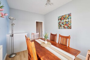 A dining area with a wooden table, four chairs, a vase with flowers, a floor lamp, and a colorful artwork on the wall. - Host Stay The Parade View (Whitby)