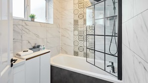 A modern bathroom with a bathtub, a glass-enclosed shower, and a vanity with a marble backsplash. - Host Stay The Parade View (Whitby)