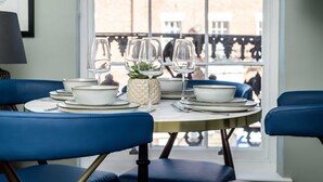A dining table set with white plates, bowls, and glasses, surrounded by blue chairs, with a window view of buildings. - Host Stay Canning Quarters I and II (Liverpool)