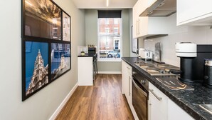 A modern kitchen with a black countertop, white cabinets, and a view of the street through a window. - Host Stay Canning Quarters I and II (Liverpool)