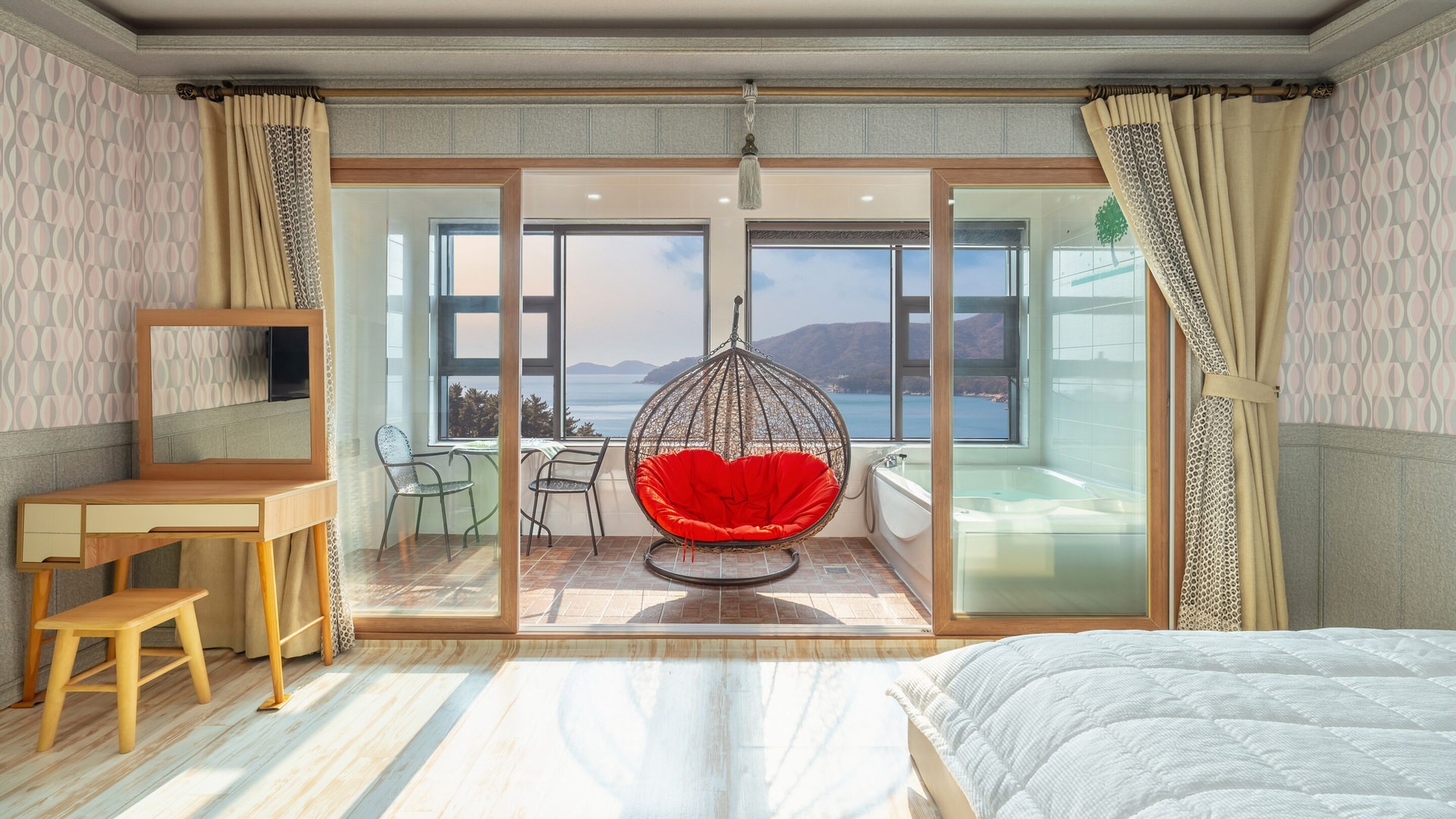 Een slaapkamer met een bed, een bureau, een stoel, een hangstoel en uitzicht op zee.