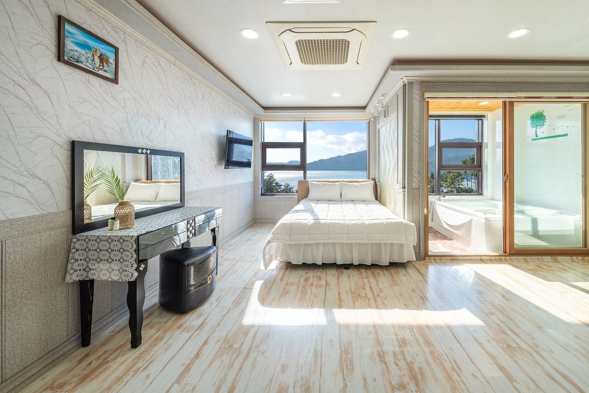 A bedroom with a bed, a desk, a TV, and a view of the outdoors.