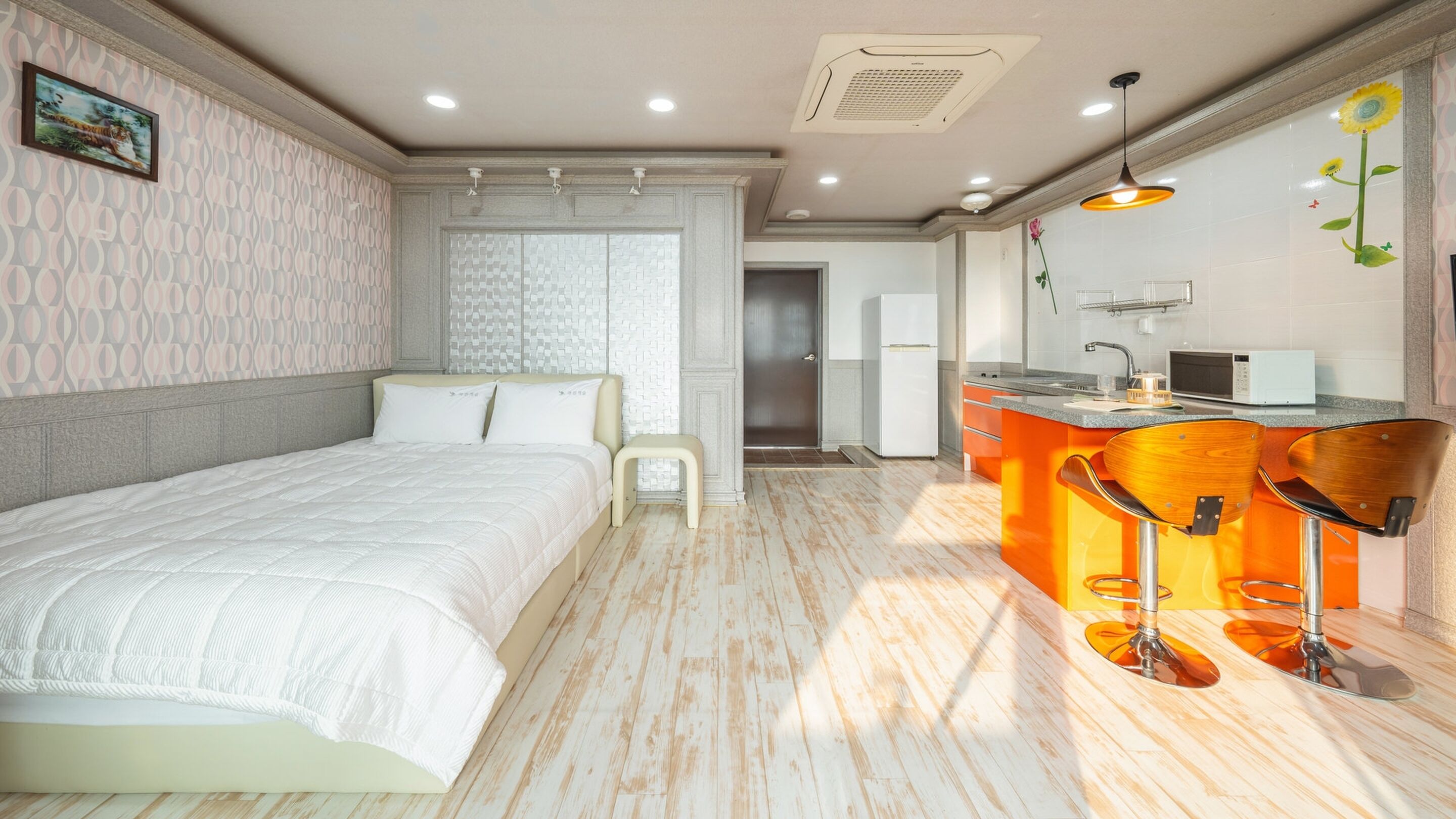 Habitación de hotel con cama, un taburete pequeño, una kitchenette con microondas y un lavabo.