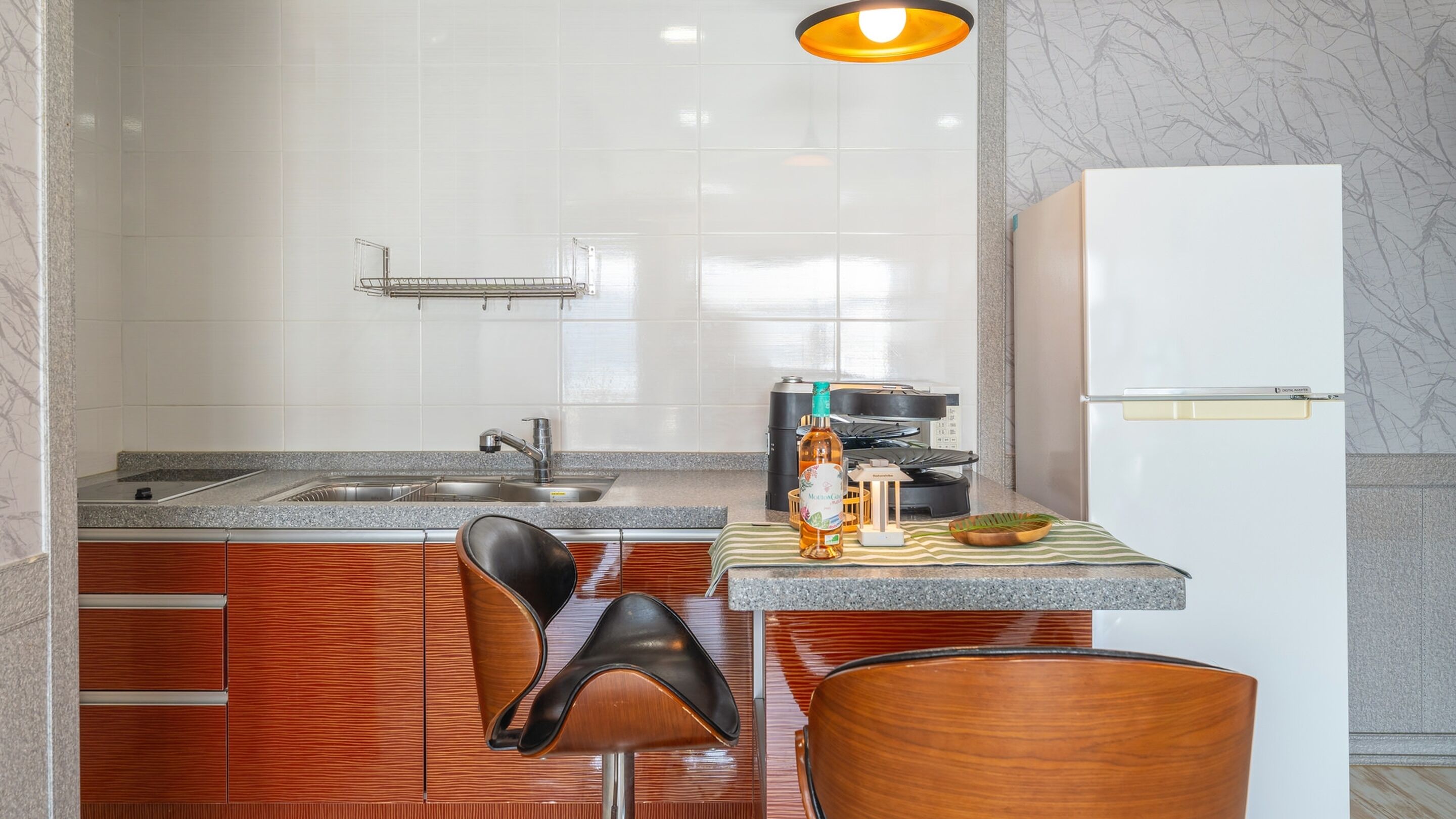 A modern kitchen with a granite countertop, stainless steel sink, and a white refrigerator.