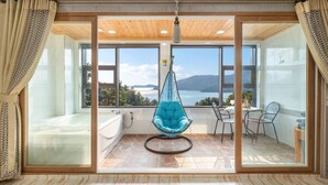 Una habitación con un ventanal grande, una silla colgante, una bañera y una zona de comedor.