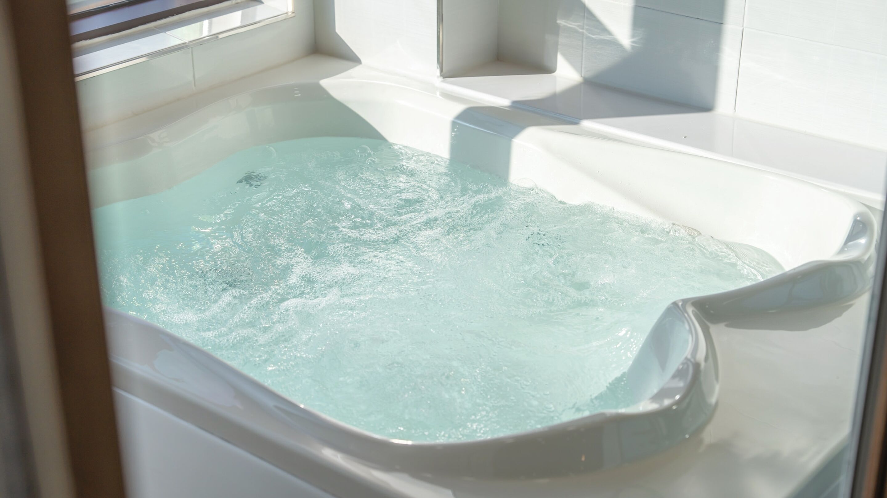 A hot tub with clear water, surrounded by white walls and a window.