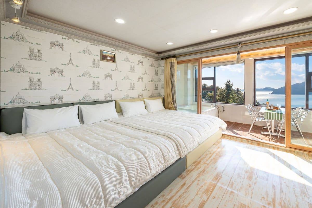A spacious bedroom with a large bed, a view of the sea, and a balcony with a table and chairs.