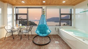 Un baño con bañera, una silla colgante y vistas a la puesta de sol sobre el agua.