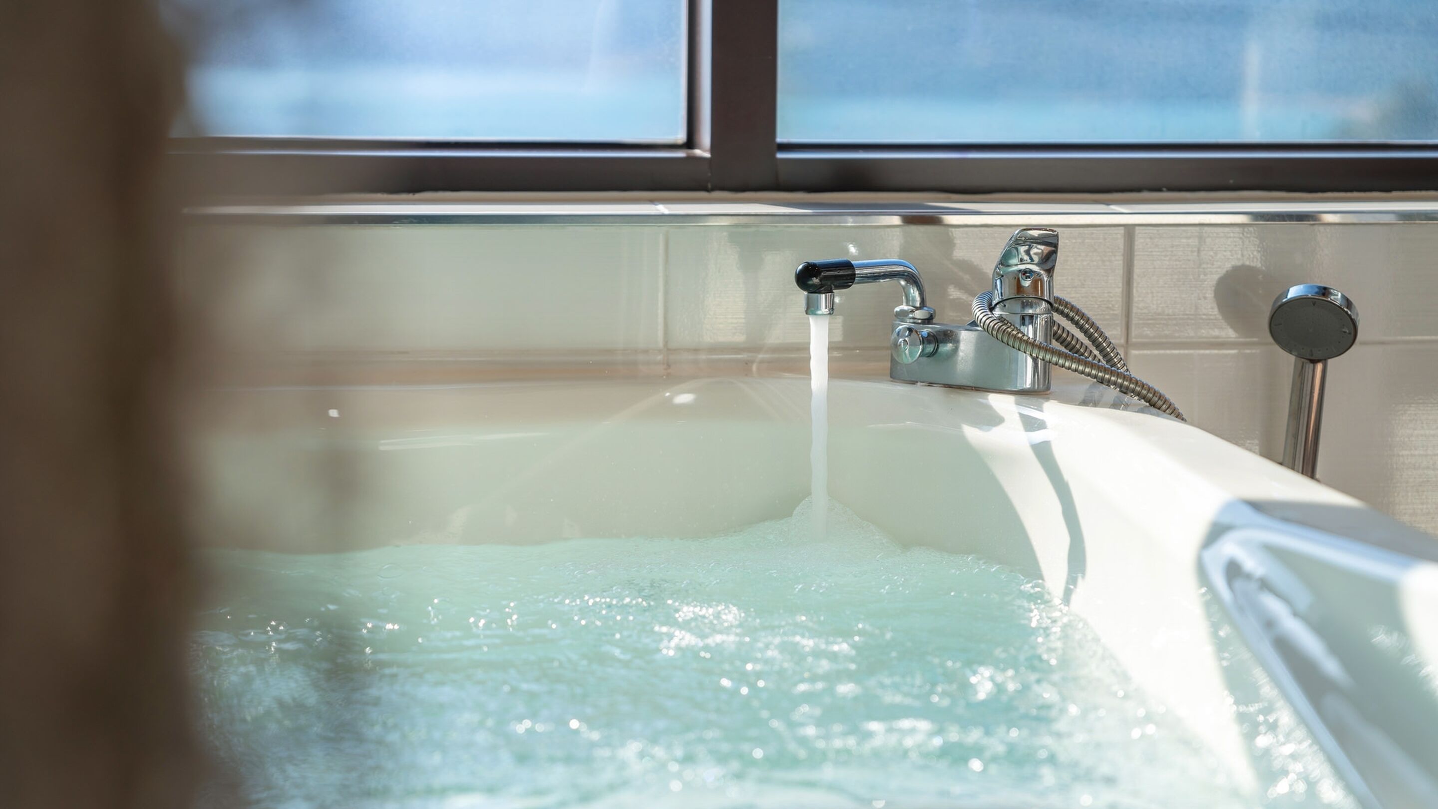 A bathtub with running water, a showerhead, and a window in the background.