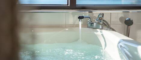 A bathtub with running water, a showerhead, and a window in the background.