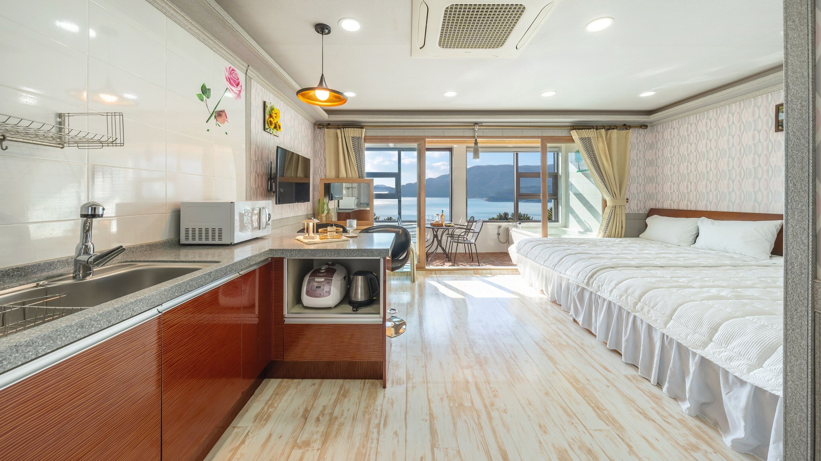 A modern hotel room with a kitchen area, a dining table, and a large bed.