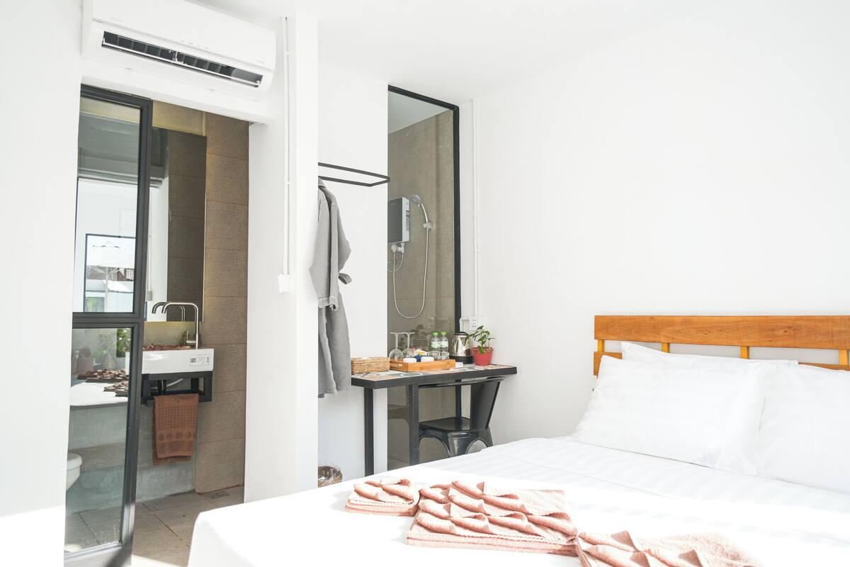 Ein Hotelzimmer mit Bett, Schreibtisch mit Spiegel, Dusche und Blick nach draußen.