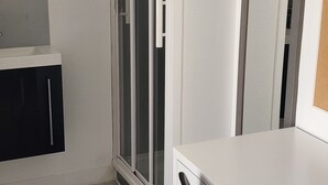 Et værelse med et hvidt skrivebord, en sort stol, en skydedør af glas og et spejl på væggen.