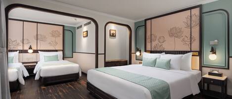 A hotel room with a large bed, two smaller beds, wooden flooring, and floral wall decor.