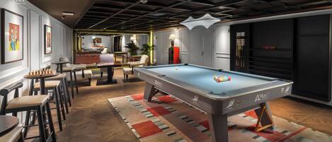 A billiards room with a pool table, chairs, and artwork on the walls.