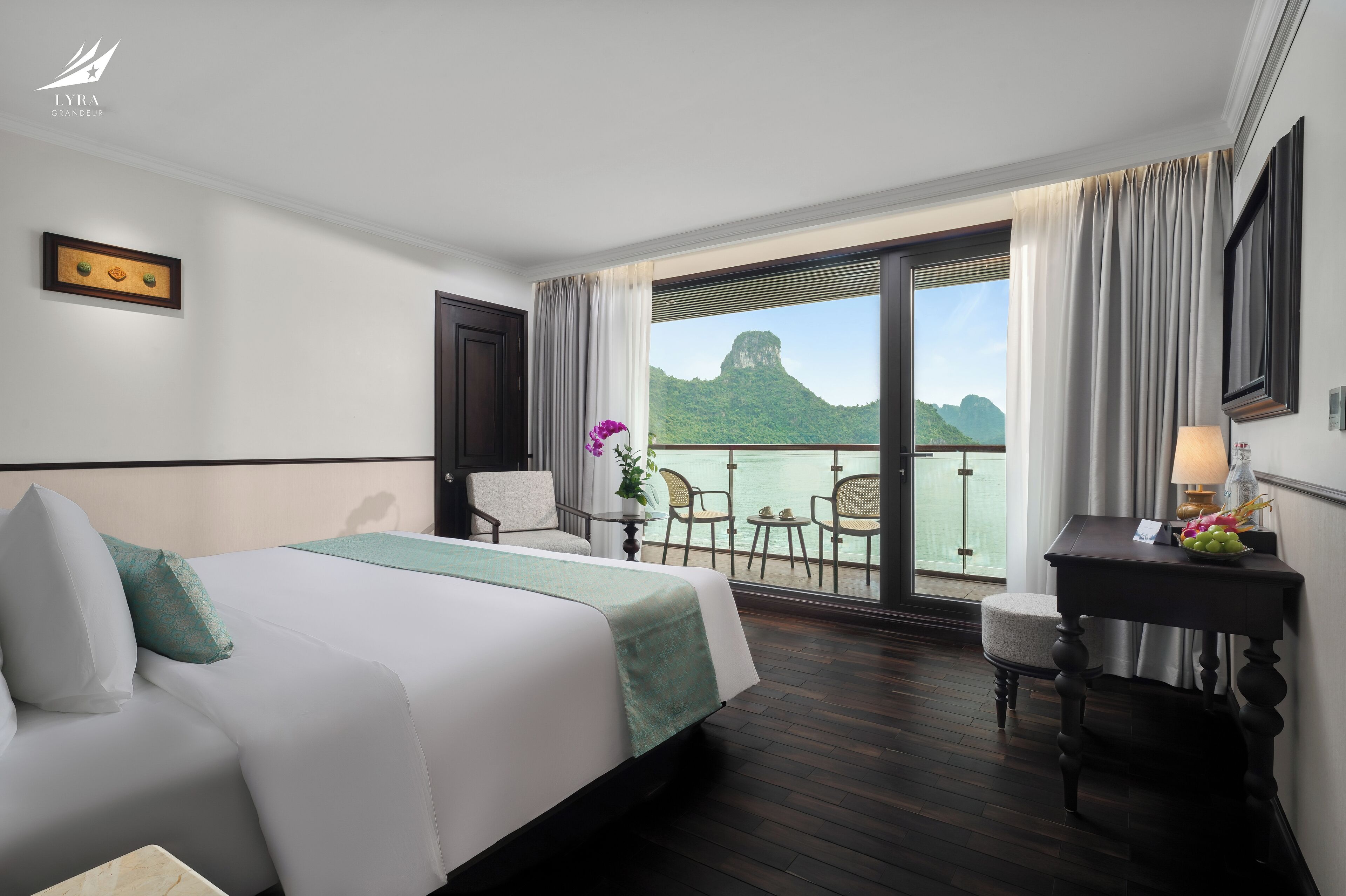 A hotel room with a bed, a desk, a chair, a table, and a view of a mountain and water.