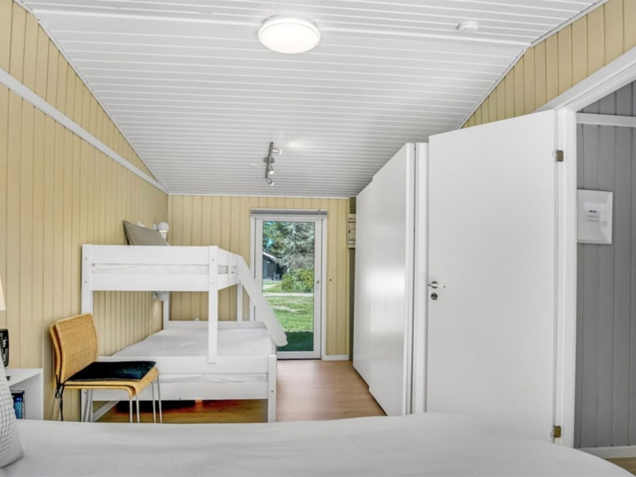 A room with a bunk bed, a desk, a chair, and a door leading to a balcony.