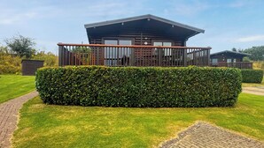 Uma pousada moderna com um deck coberto, gramado bem cuidado e um hedge em primeiro plano.