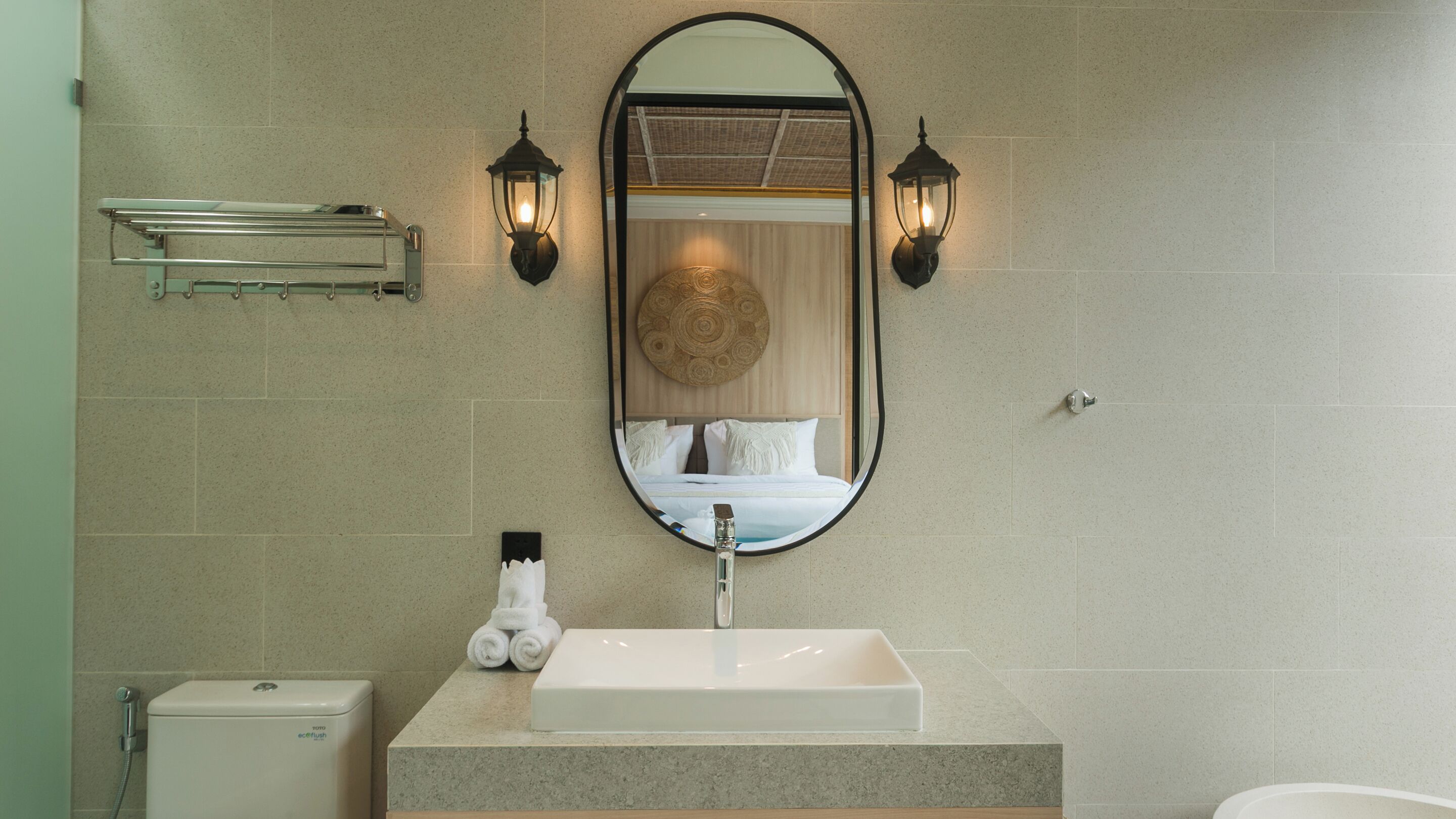 A bathroom with a large oval mirror, a white sink, and two wall-mounted lights.