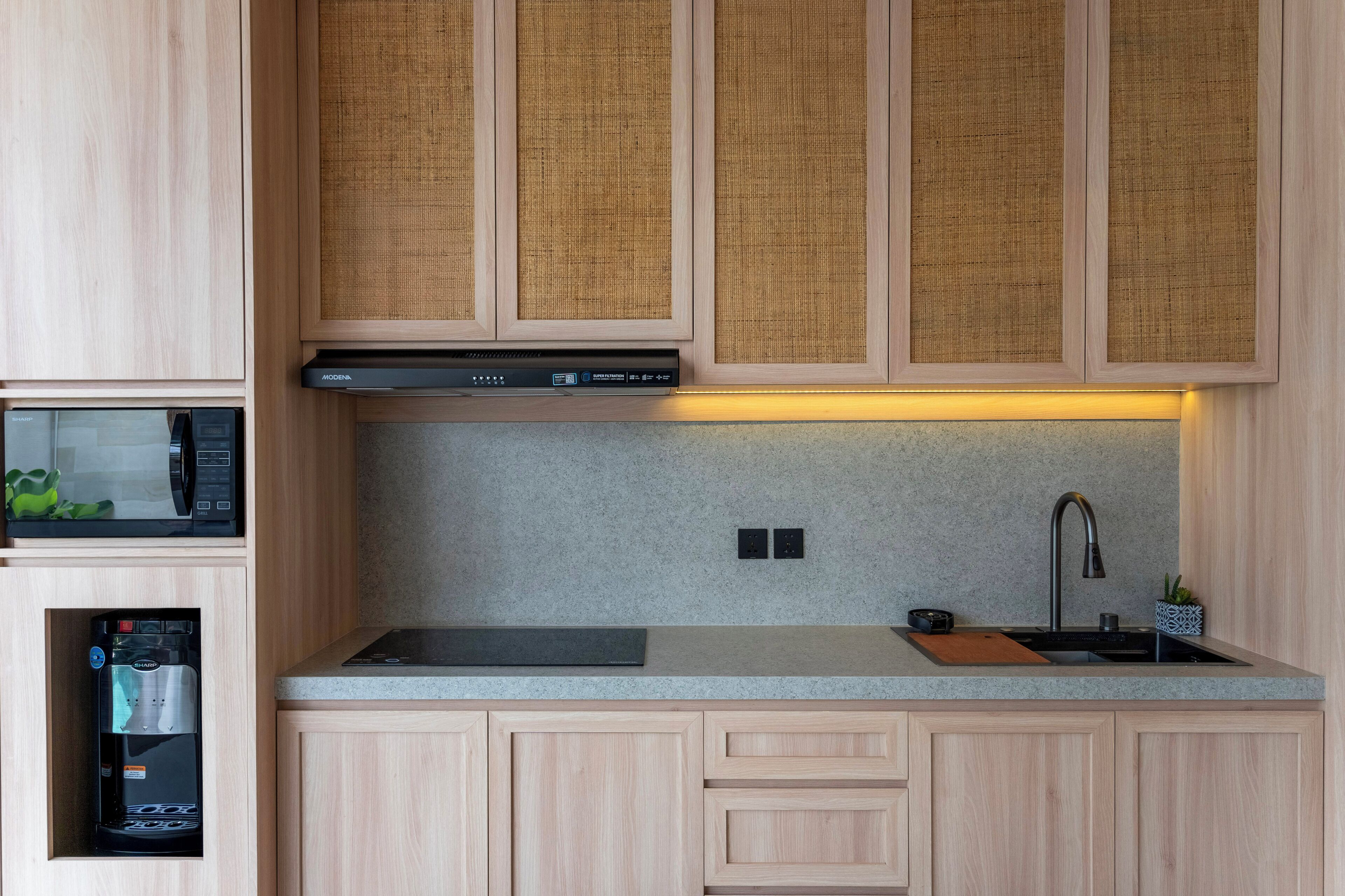 Una cocina moderna con armarios de madera, microondas integrado, cafetera y pileta de acero inoxidable.
