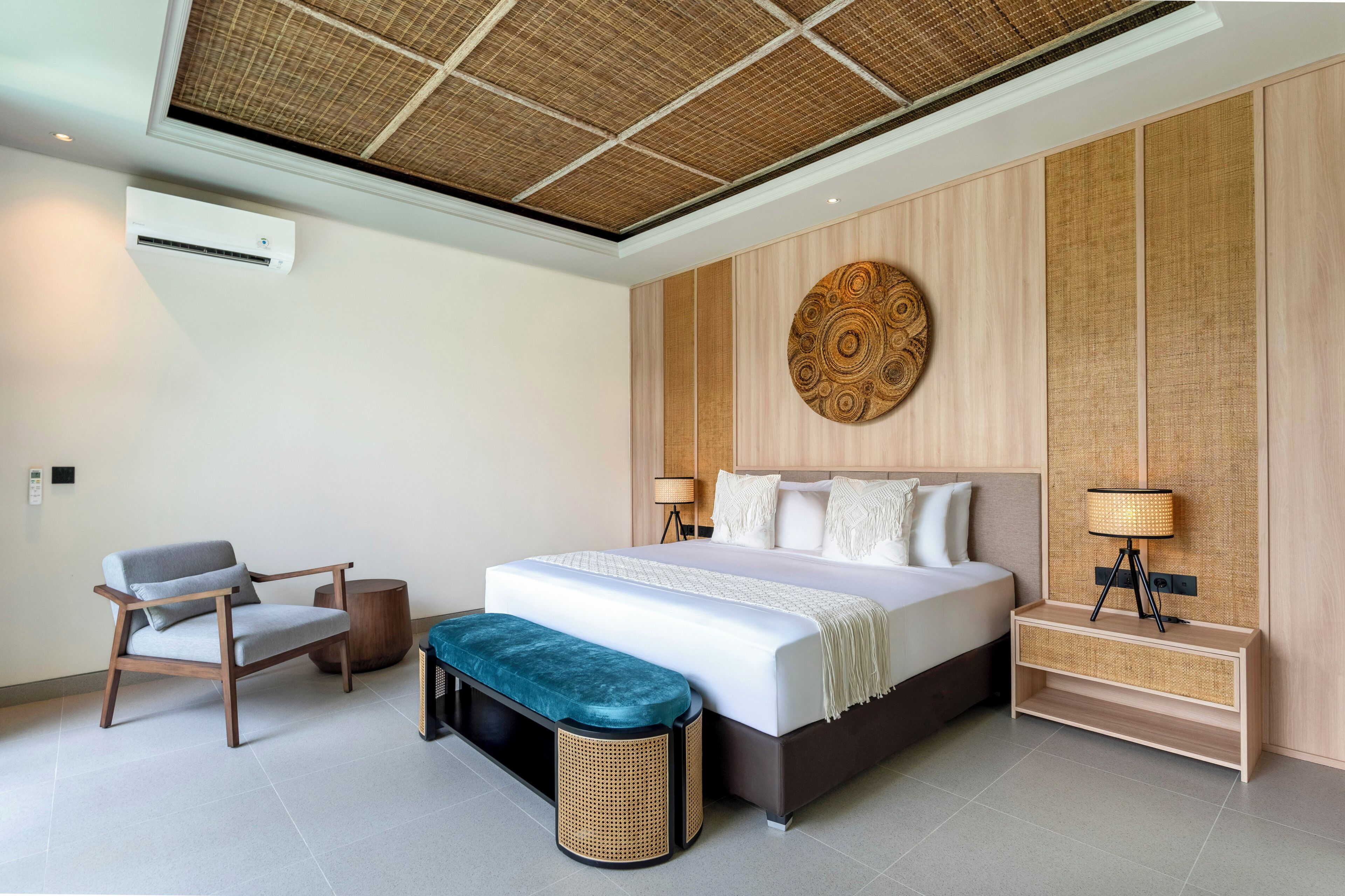 A modern bedroom with a large bed, a bedside table with a lamp, a chair, and a bench.