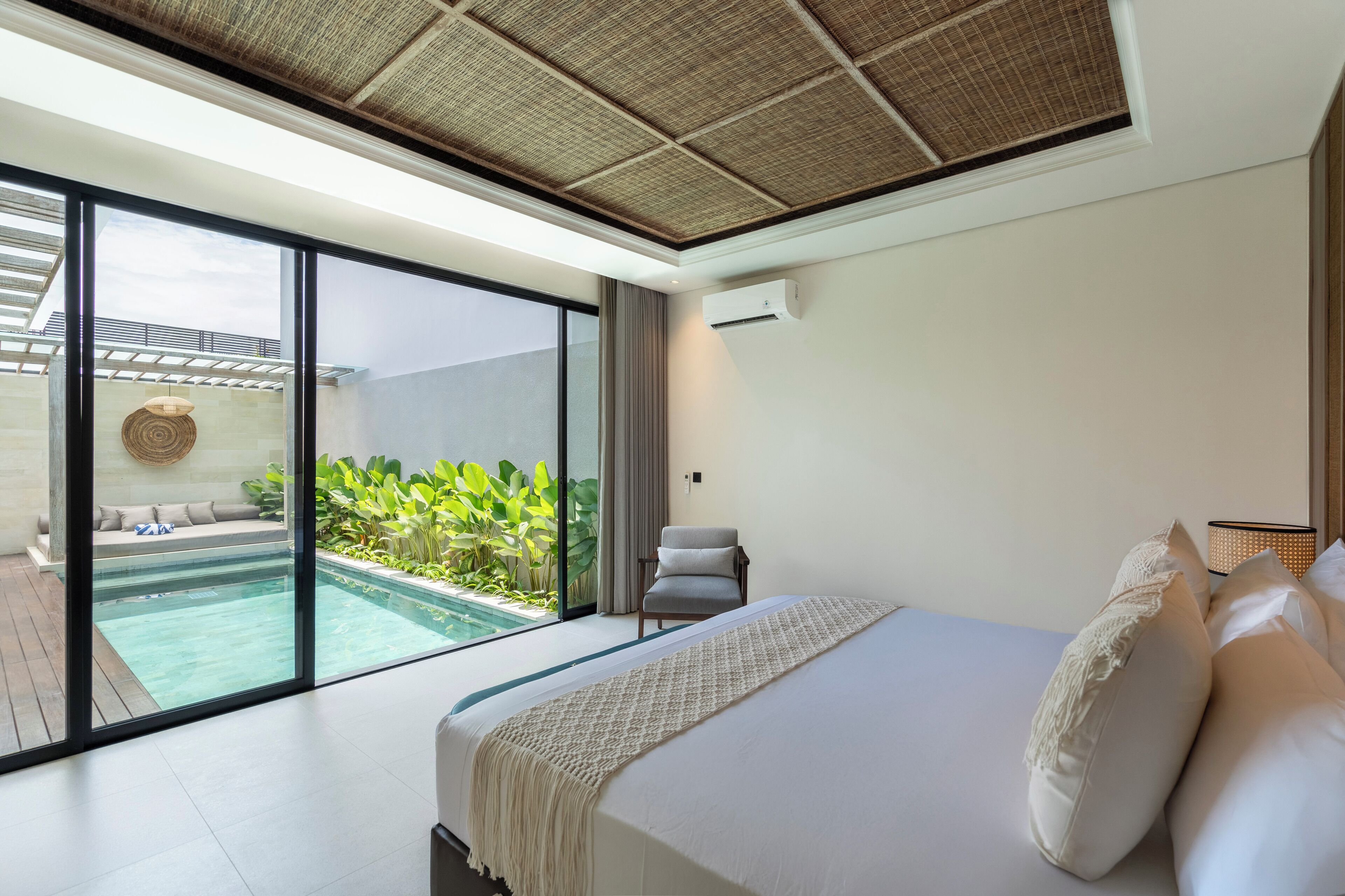 A modern bedroom with a large bed, a view of a swimming pool, and a ceiling with a woven design.