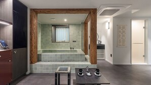 Un baño moderno con una bañera independiente, un espejo y una mesita con vasos y una jarrón.