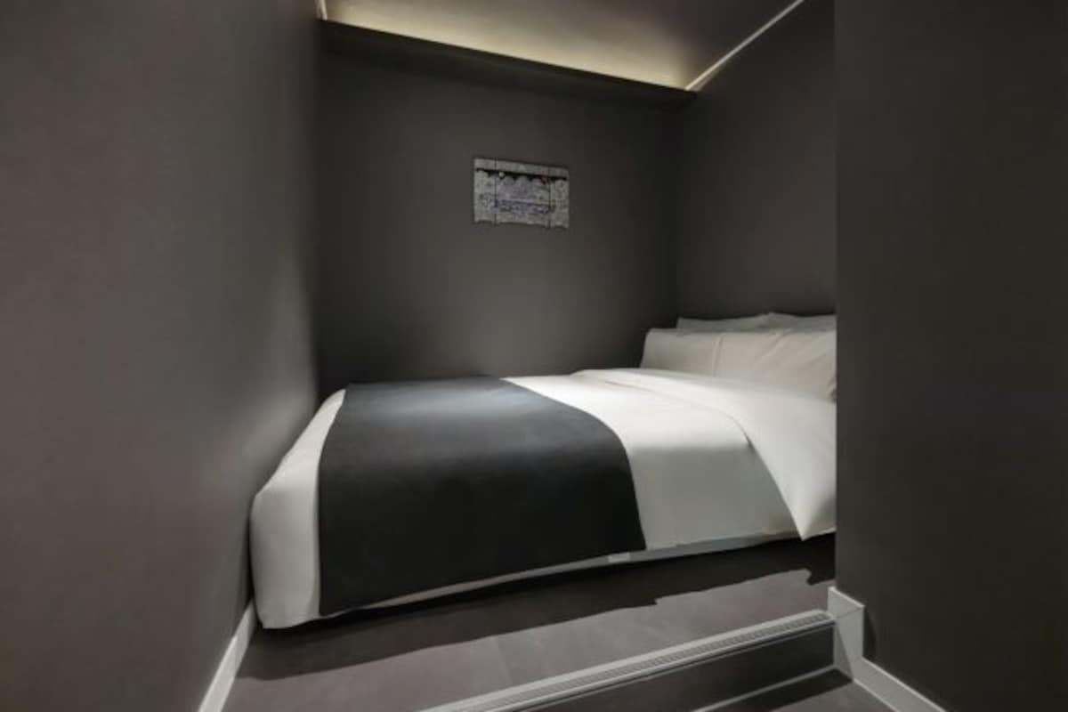A modern bedroom with a bed, dark walls, and a small poster on the wall.