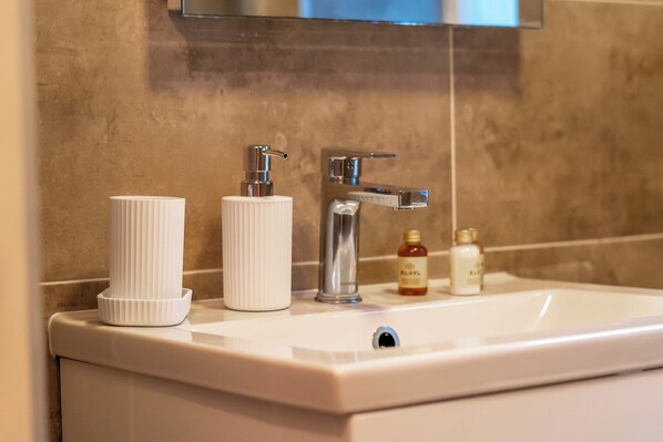 A bathroom sink with a white basin, a chrome faucet, and two toiletries: a white bottle and a smaller amber bottle.