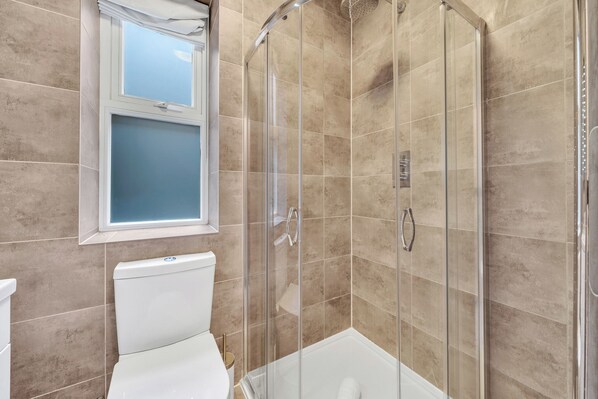 Un bagno con doccia vetro, toilette e finestra sopra il lavandino.