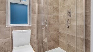 Un baño con ducha de vidrio, inodoro y ventana.
