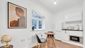Una cocina moderna con armarios blancos, microondas y un pequeño comedor con una mesa redonda y dos sillas.