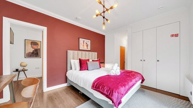 Un dormitorio con cama, escritorio, silla, armario y candelabro.