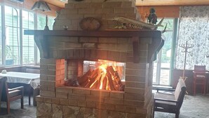 A stone fireplace with a fire, surrounded by wooden logs and a deer head decoration. - Rahat  (Khachmaz)