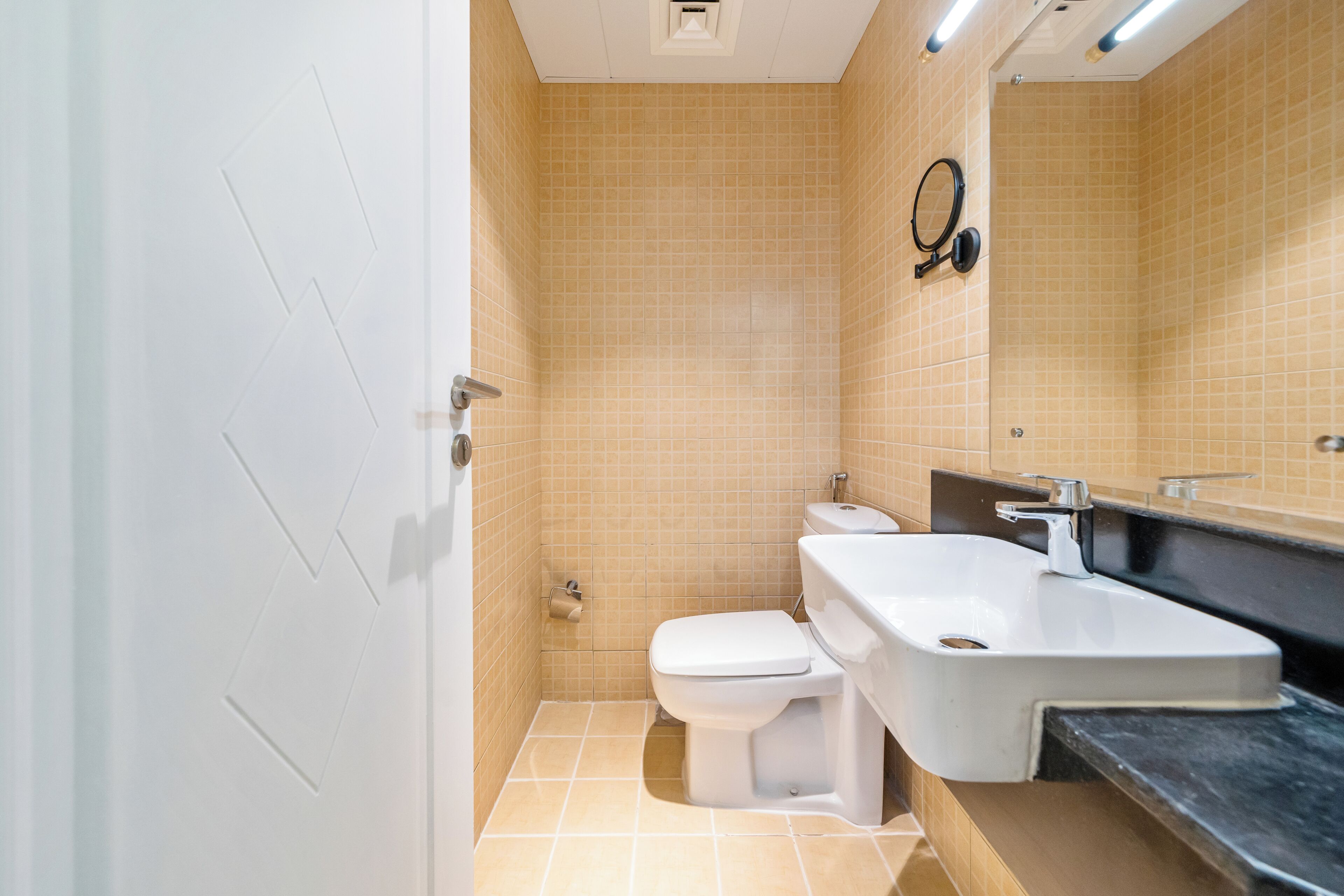 Et badeværelse med toilet, vask og spejl.