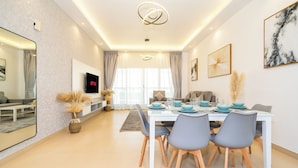 A modern dining area with a white table set for four, grey chairs, and a flat-screen TV mounted on the wall. - Zapbed House - SP 803 (Dubai)
