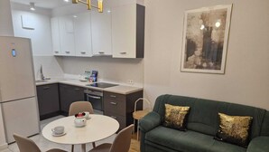 Eine moderne Küche mit weißen Schränken, einem Esstisch mit Stühlen, einem grünen Sofa mit Zierkissen und einem gerahmten Bild an der Wand.