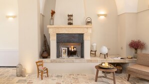 Une pièce chaleureuse avec une cheminée en pierre, une chaise en bois, une petite table et un canapé en osier.