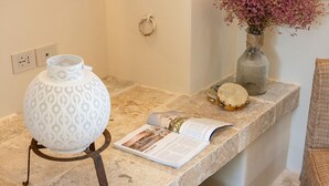 Un meuble-lavabo de salle de bain agrémenté d’une lampe à motifs, d’un vase avec des fleurs et d’un livre posé sur le plan de travail.