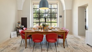 Un coin repas avec une grande fenêtre, une table en bois dressée pour six personnes et des chaises rouges.