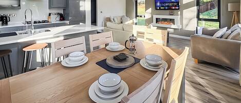 A modern kitchen with a central island, bar stools, a dining table set with plates, and a TV mounted on the wall.