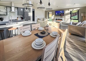 Una cocina moderna con una isla central, taburetes de bar, una mesa de comedor con platos y un televisor montado en la pared.