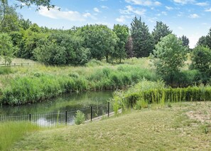 Un parc paisible situé au bord de la rivière, agrémenté d’une clôture en métal, d’une végétation luxuriante et d’arbres.