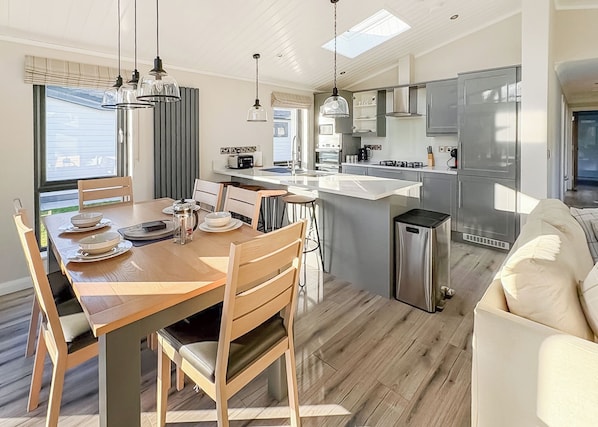 Une cuisine moderne dotée d’un îlot central, d’appareils électroménagers en acier inoxydable et de luminaires suspendus.