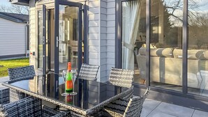 A modern outdoor dining area with a glass table, wicker chairs, and a bottle of champagne. - 3 bedroom accommodation in Faringdon (Faringdon)