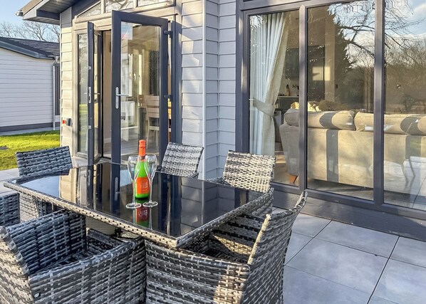 A modern outdoor dining area with a glass table, wicker chairs, and a bottle of champagne. - 1 bedroom accommodation in Faringdon (Faringdon)