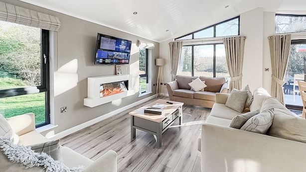 A modern living room with a fireplace, a television mounted on the wall, and large windows. - 3 bedroom accommodation in Faringdon (Faringdon)